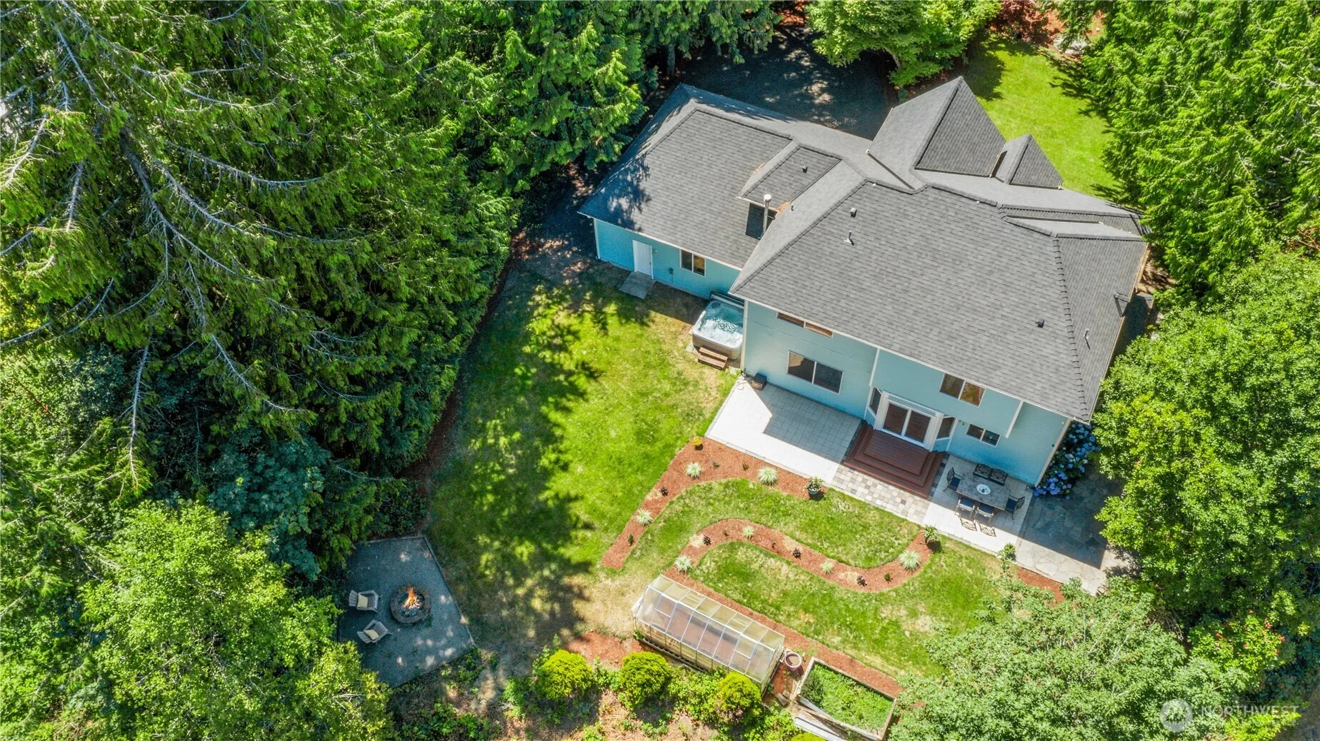 From above: a grey roof and a lawn cut into a forest of tall evergreens.