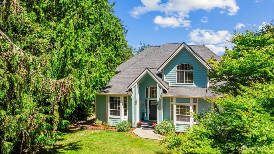 Turquoise two-story house among evergreens on a wide lawn.