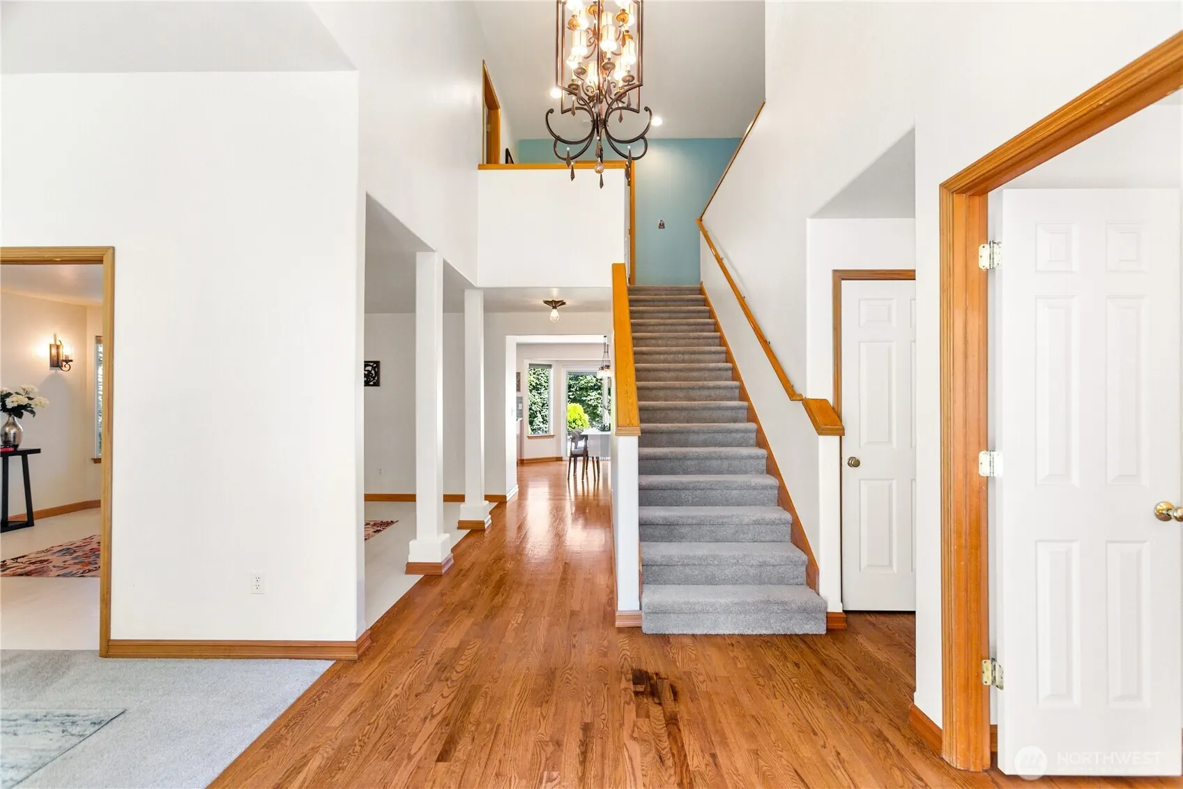 Entry hall with hardwood floors, a staircase rising under a vaulted ceiling and a chandelier.
