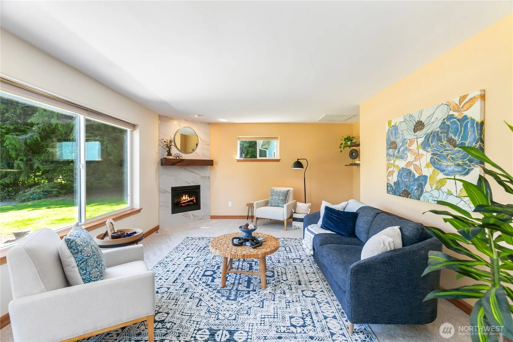 Family room with a corner fireplace, a navy sofa and wide windows onto the trees.