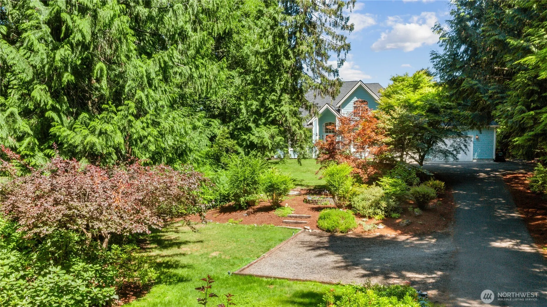 From above: a garden path curving between flowering shrubs toward the house under tall evergreens.
