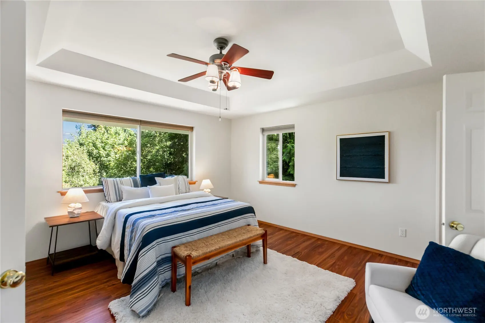 Primary bedroom with a tray ceiling, ceiling fan and large window.
